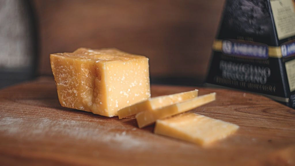 Dettaglio della crosta di una forma di Parmigiano Reggiano con marchio a fuoco del caseificio e timbro ovale del Consorzio DOP